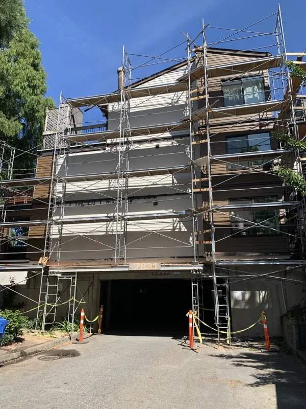 A multi-story building undergoing building envelope restoration, covered in scaffolding with caution tape and traffic cones at the entrance.