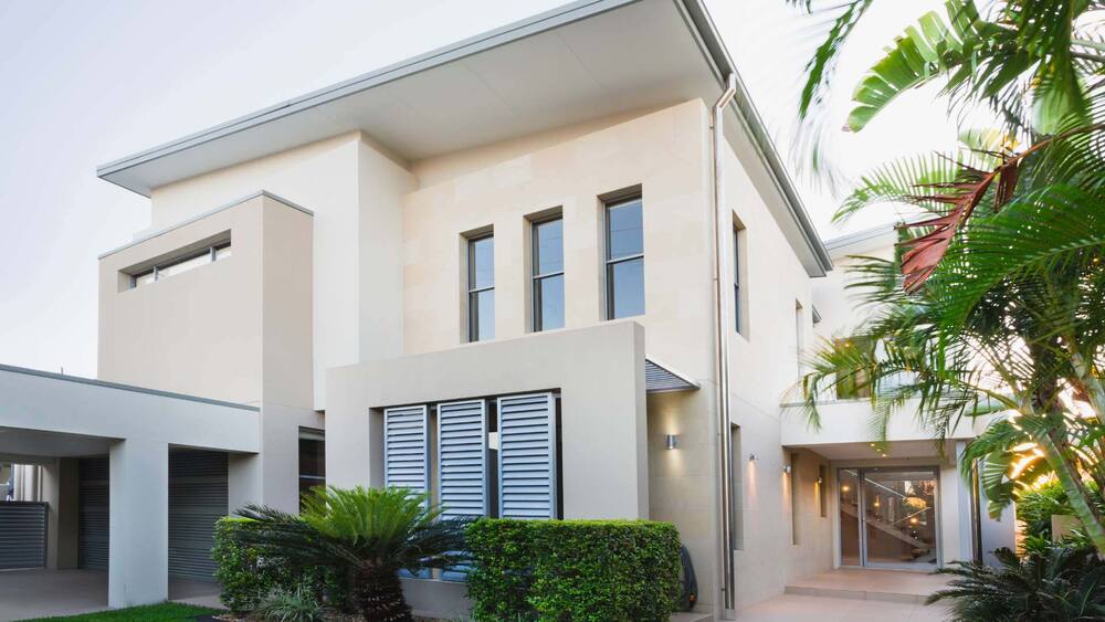Modern two-story house with large windows, beige exterior, and surrounding palm trees features exceptional flooring installation throughout.