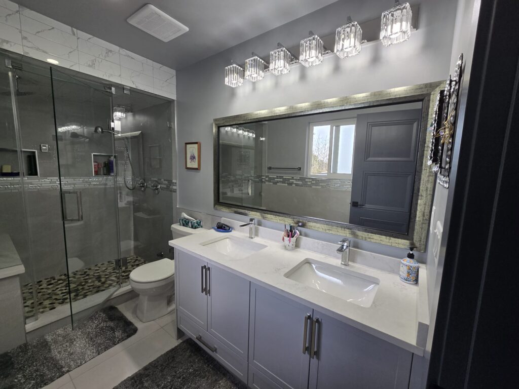 Modern bathroom with double sink vanity, large mirror, wall lighting, glass shower enclosure, and gray and white decor—expertly maintained with top-tier property maintenance for lasting style and comfort.