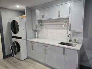 Modern laundry room with stacked washer and dryer, light gray cabinets, white hexagon tile backsplash, and a stainless steel sink—ideal for easy property maintenance.