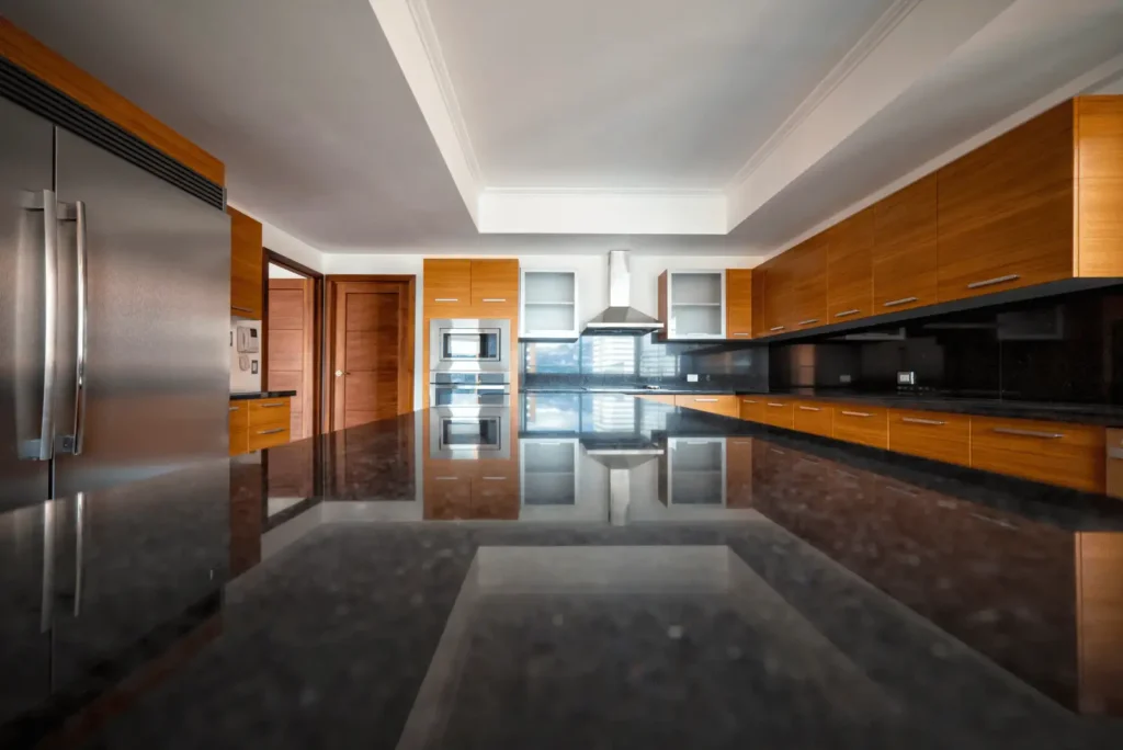 Modern kitchen with stainless steel appliances, wooden cabinets, a black granite countertop, and a center island reflecting the room's features.
