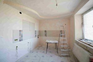 A room under renovation with unfinished walls, a step ladder, a table with tools, exposed wiring, and a large window letting in natural light—perfect inspiration for budget-friendly home renovation ideas for Coquitlam homes.