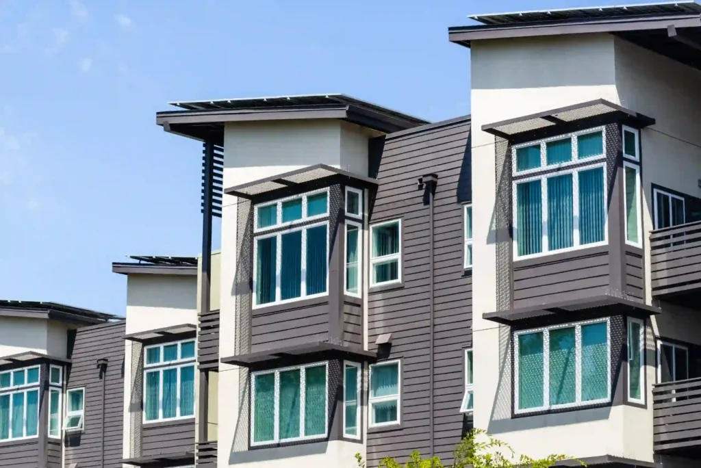 Modern apartment building with large windows, gray siding, and white trim under a clear blue sky.